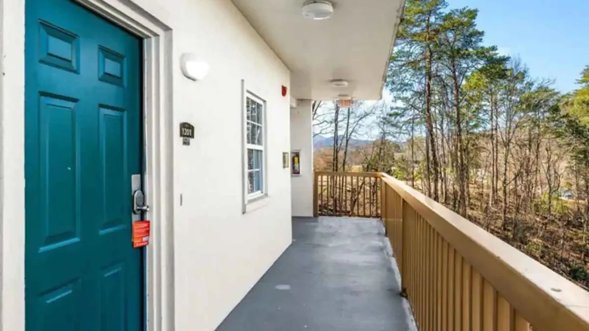 A welcoming exterior view of the condo’s teal door and wooden railing, surrounded by lush trees. The setting is peaceful and inviting, ideal for savoring a quiet morning coffee or sharing an intimate moment outdoors. The natural light and greenery set a romantic and tranquil mood.