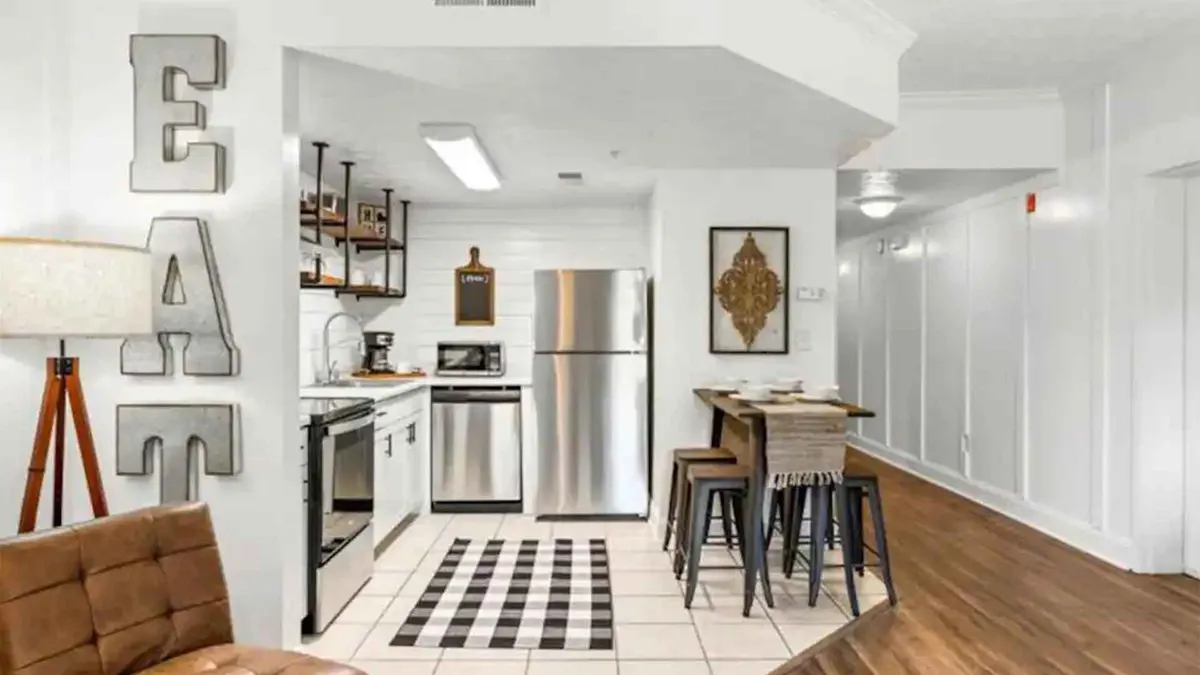 An open kitchen and dining space with a well-appointed kitchen area, a stylish dining table set for a meal, decorative wall art, and a softly glowing lamp that creates a welcoming ambiance. The layout encourages socializing and shared meals.