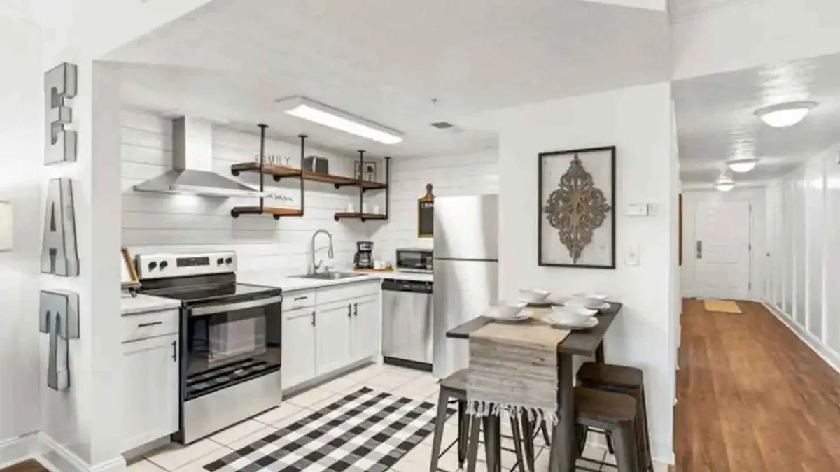 The image shows a beautifully remodeled kitchen and dining area with modern appliances, open shelving, and a welcoming dining table, all set within a cozy, thoughtfully designed condo. The setting suggests a space perfect for cooking, entertaining, and enjoying meals together.