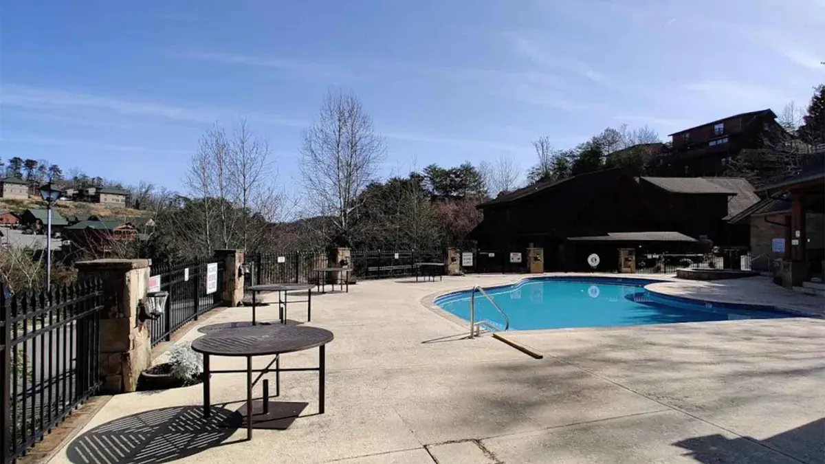 An exterior shot of the resort’s swimming pool area, complete with a seating area, surrounding trees, and a secure fence. The atmosphere is tranquil and perfect for couples wishing to unwind together, whether swimming, sunbathing, or simply enjoying the peaceful ambiance.