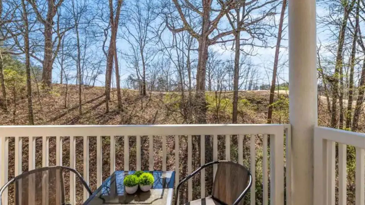 A private deck with comfortable outdoor seating, bordered by a wooden railing and adorned with small potted plants. The space opens out to a peaceful natural landscape, inviting guests to relax while enjoying the sounds and sights of nature.