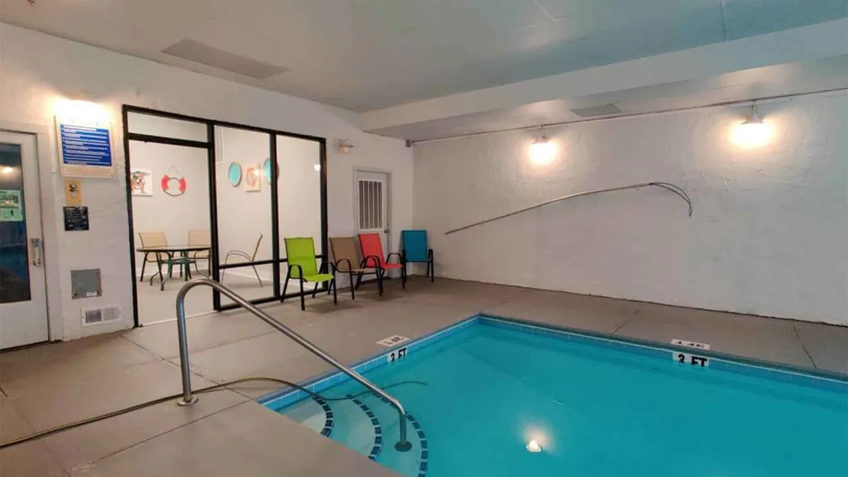 A tranquil indoor swimming pool with colorful chairs and inviting pool steps. The serene atmosphere is complemented by natural light streaming through large windows, creating a peaceful space for relaxation or gentle swims.