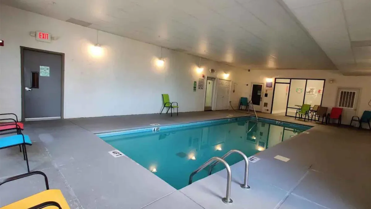 A bright and inviting indoor swimming pool area with colorful lounge chairs arranged along the pool deck. Large windows let in ample natural light, while guests can be seen relaxing and socializing. The space feels open and lively, perfect for leisure and family fun.