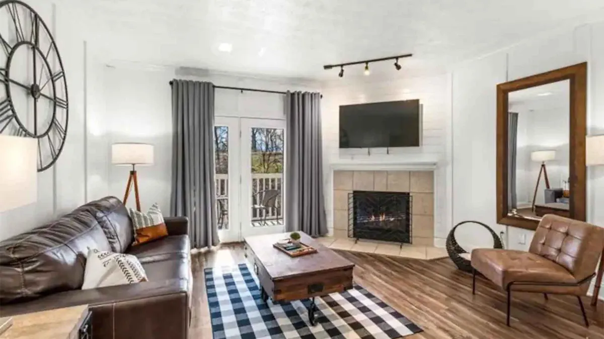 A comfortable living space with a leather sofa arranged around a fireplace, a modern coffee table, a large mirror, and a television. The room is bathed in natural light, offering a cozy setting for both socializing and quiet moments.